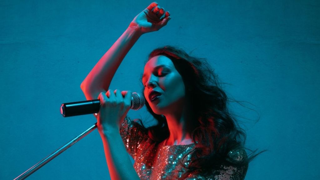 Female singer performing passionately with a microphone under dramatic stage lighting.