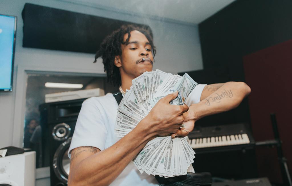Music artist holding money stacks in a studio, representing the debate about royalties and fair pay in AI vocals.